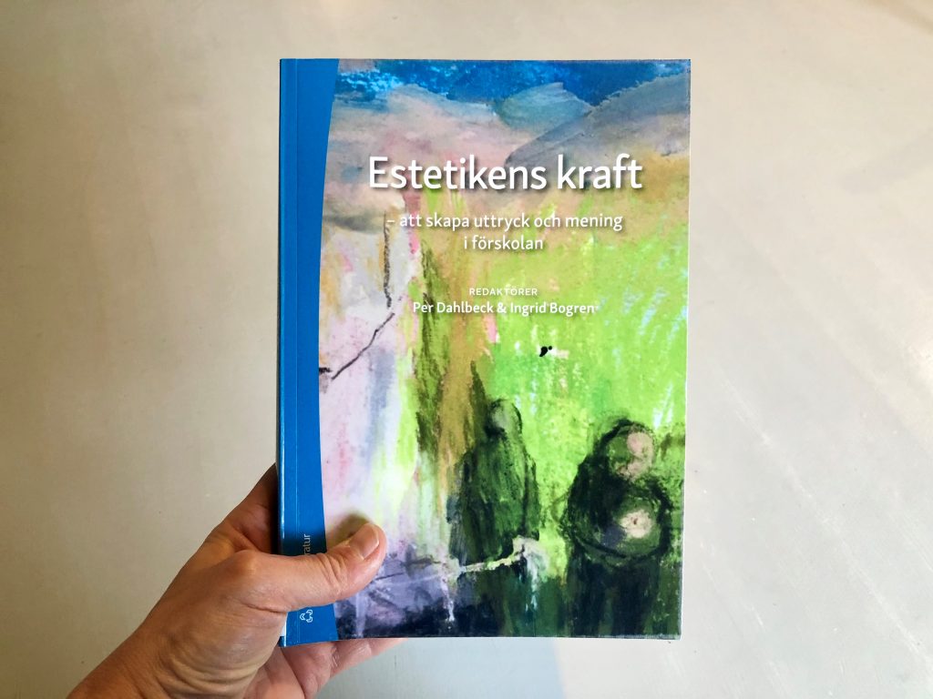 En hand håller i boken Estetikens kraft - att skapa uttryck och mening i förskolan